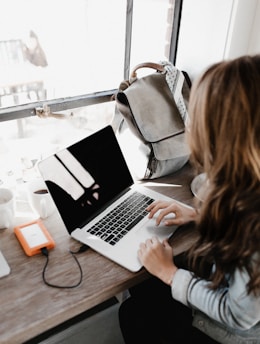 girl wearing grey long-sleeved shirt using MacBook Pro on brown wooden table