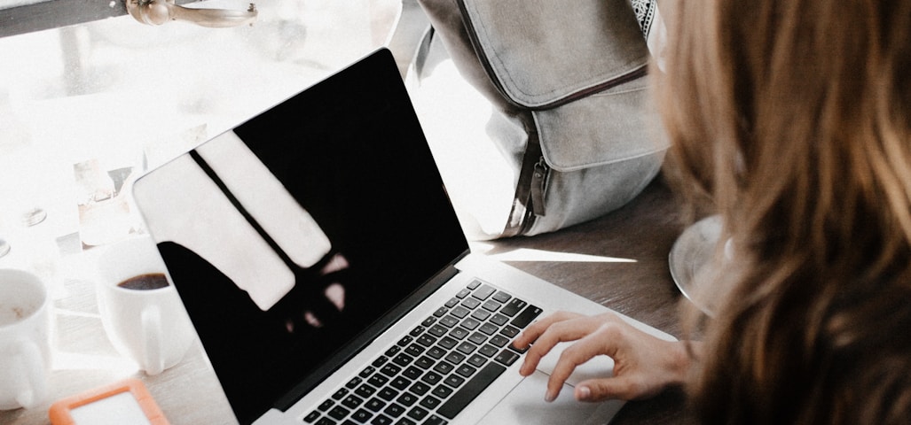 girl wearing grey long-sleeved shirt using MacBook Pro on brown wooden table