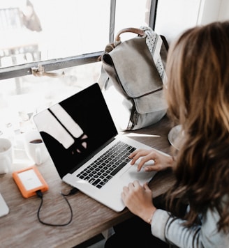 girl wearing grey long-sleeved shirt using MacBook Pro on brown wooden table