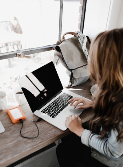 girl wearing grey long-sleeved shirt using MacBook Pro on brown wooden table