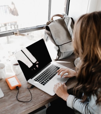 girl wearing grey long-sleeved shirt using MacBook Pro on brown wooden table