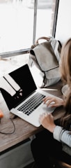 girl wearing grey long-sleeved shirt using MacBook Pro on brown wooden table