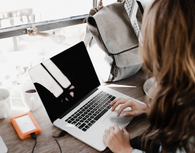 girl wearing grey long-sleeved shirt using MacBook Pro on brown wooden table