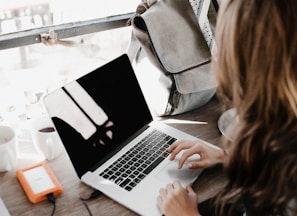 girl wearing grey long-sleeved shirt using MacBook Pro on brown wooden table