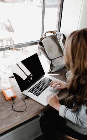 girl wearing grey long-sleeved shirt using MacBook Pro on brown wooden table