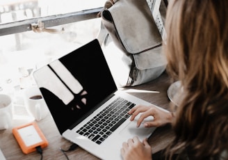 girl wearing grey long-sleeved shirt using MacBook Pro on brown wooden table