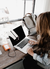 girl wearing grey long-sleeved shirt using MacBook Pro on brown wooden table