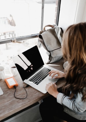 girl wearing grey long-sleeved shirt using MacBook Pro on brown wooden table