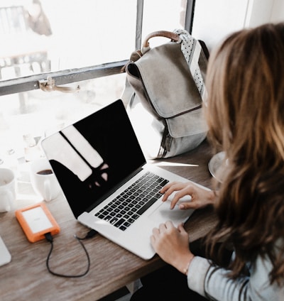 girl wearing grey long-sleeved shirt using MacBook Pro on brown wooden table