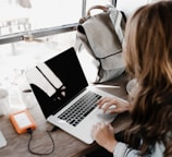 girl wearing grey long-sleeved shirt using MacBook Pro on brown wooden table