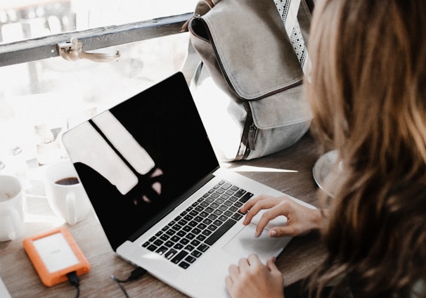 girl wearing grey long-sleeved shirt using MacBook Pro on brown wooden table