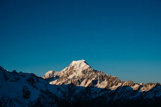 A crisp, sunlit mountain peak with a clear blue sky backdrop, capturing the essence of freedom and elevation.
