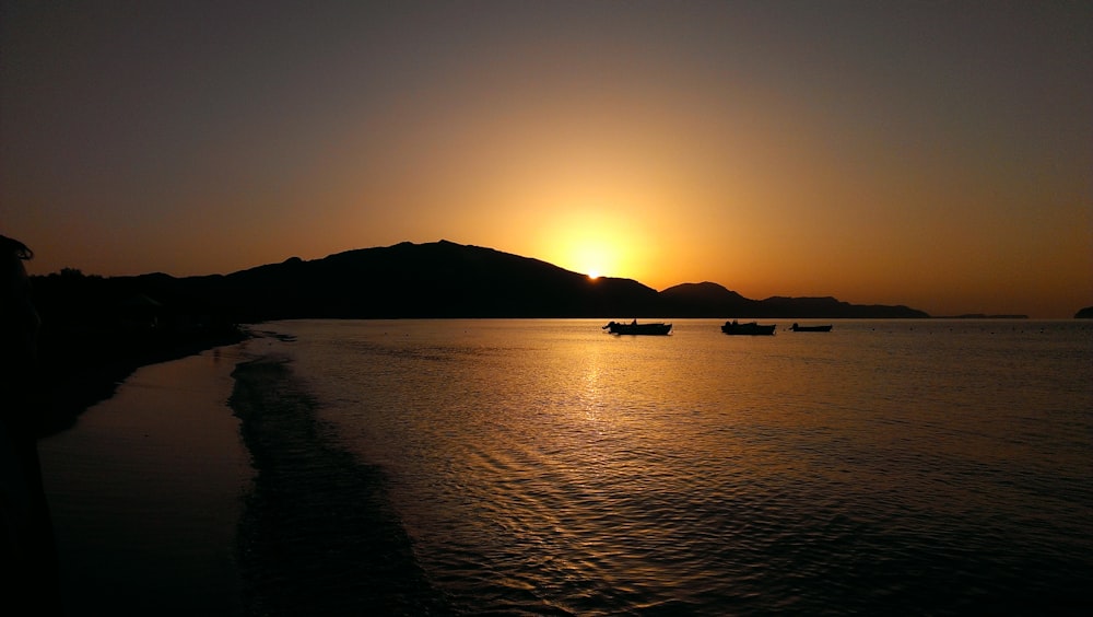 three boat sailing on ocean near shore during sunset