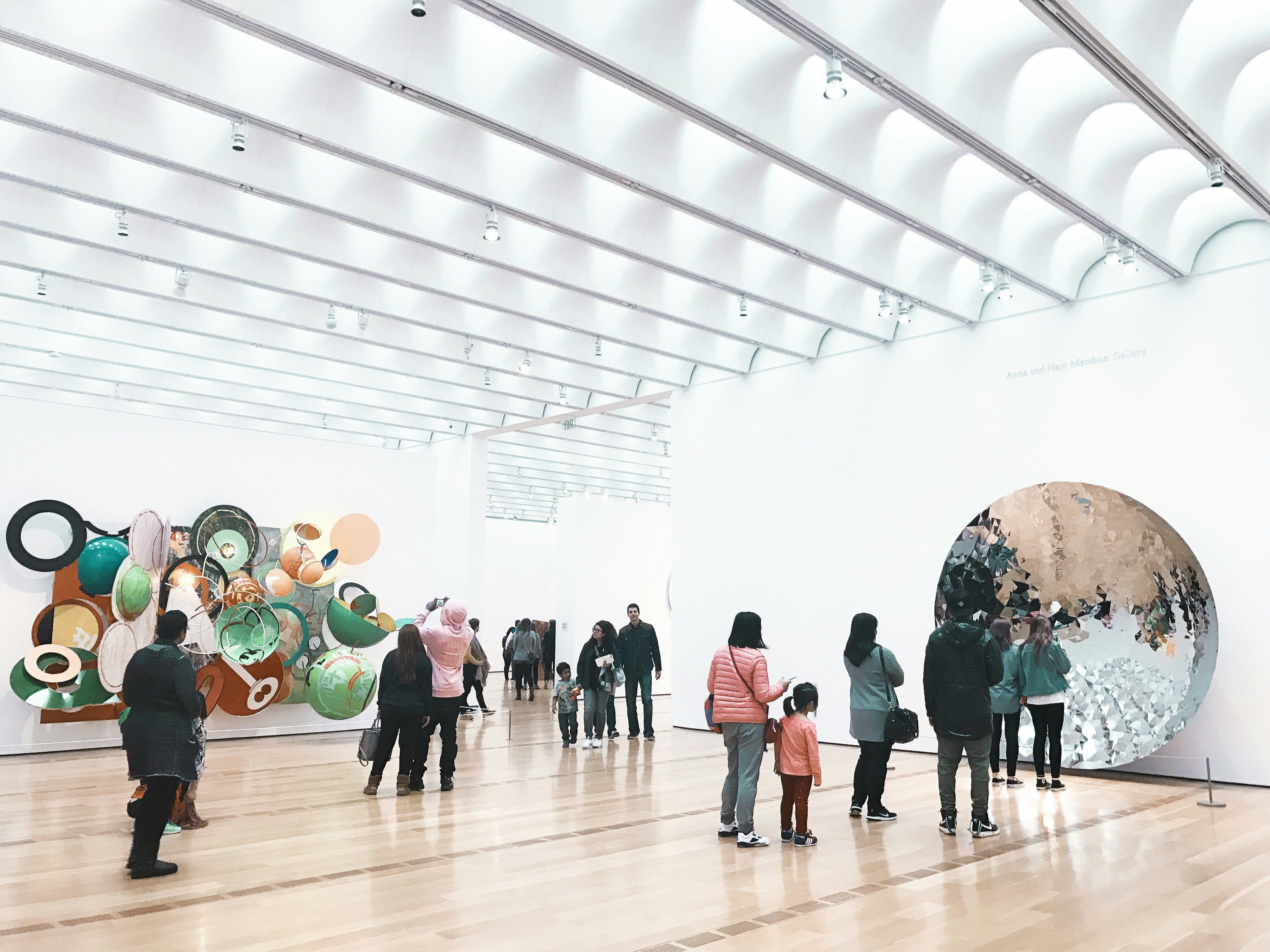 Visitors viewing large paintings in bright white gallery space, open natural lighting
