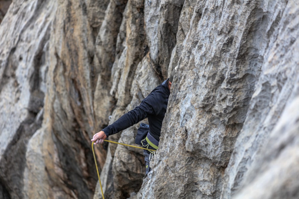 Hombre con chaqueta negra escalando en la montaña de roca gris durante el día