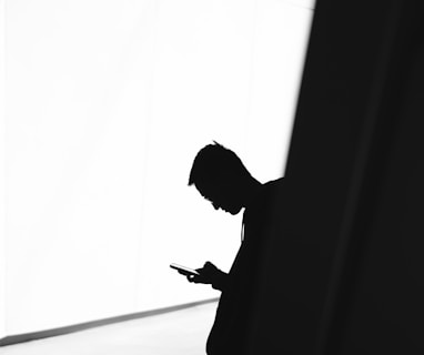 person using phone leaning on wall in silhouette photography