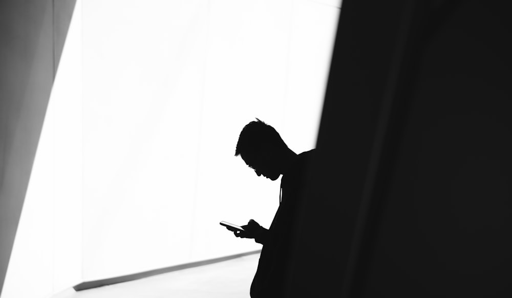 person using phone leaning on wall in silhouette photography