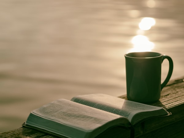 An open book sitting next to a mug.