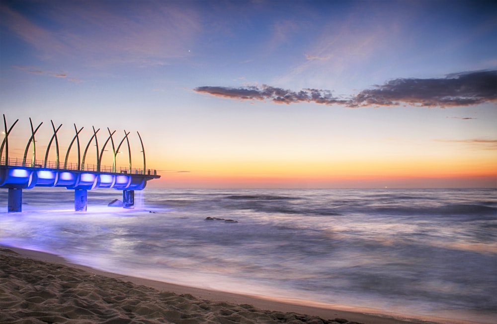 a pier on the beach at sunset with blue lights