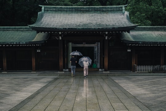 two people holding umbrellas near brown building during rainy season in Meiji Shrine Japan