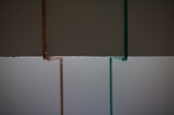 Two vertical pipes, one copper-colored and the other teal, are on a background that is divided horizontally, with dark gray on top and light gray below.