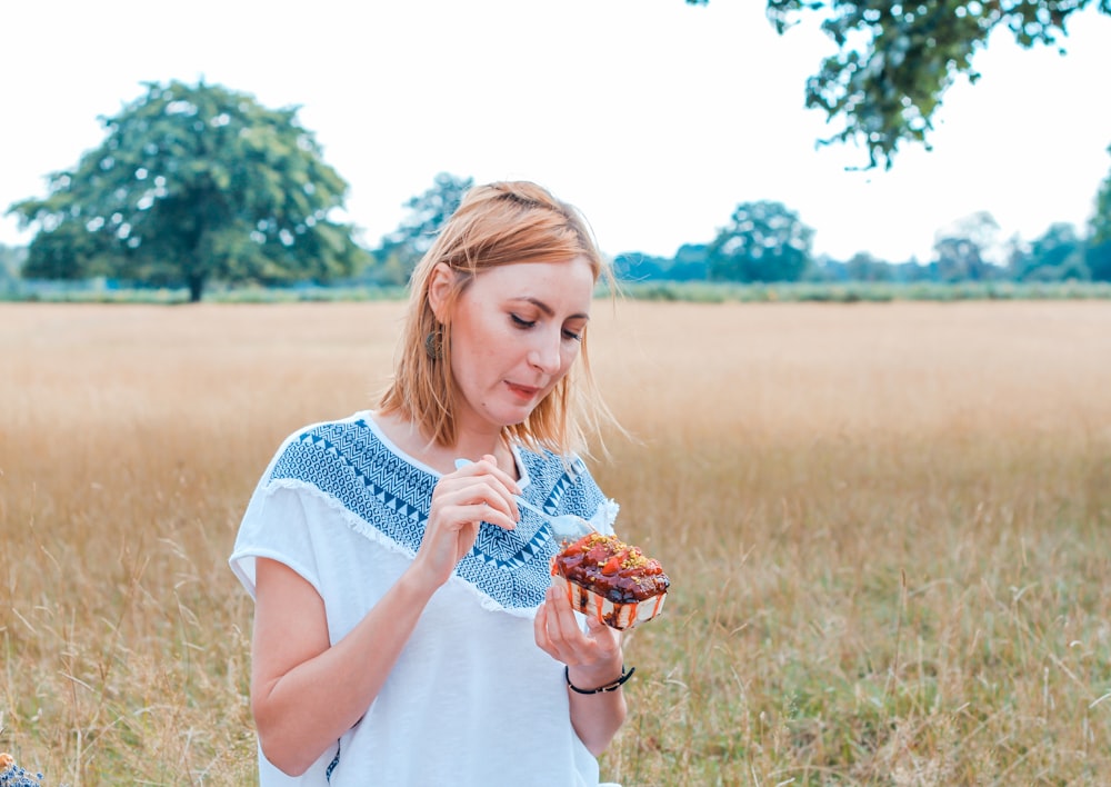 shallow focus photo of woman in white and blue T-shirt eating dessert