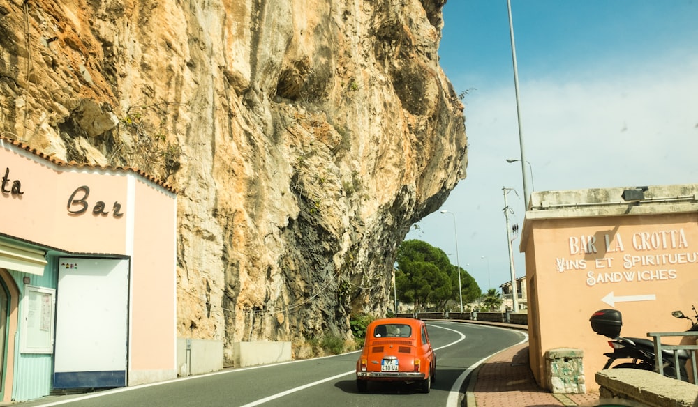 coupé rosso Volkswagen Beetle sulla strada di cemento nero tra gli edifici in calcestruzzo sotto il cielo bianco e blu di giorno