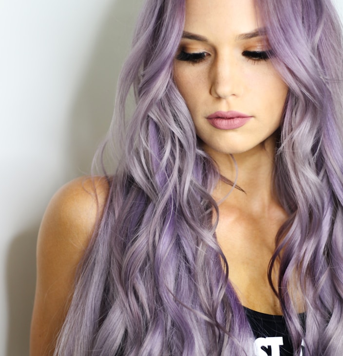 purple haired woman in black top leaning on wall