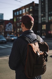 man wearing black jacket and cap standing near road looking forward