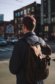 man wearing black jacket and cap standing near road looking forward