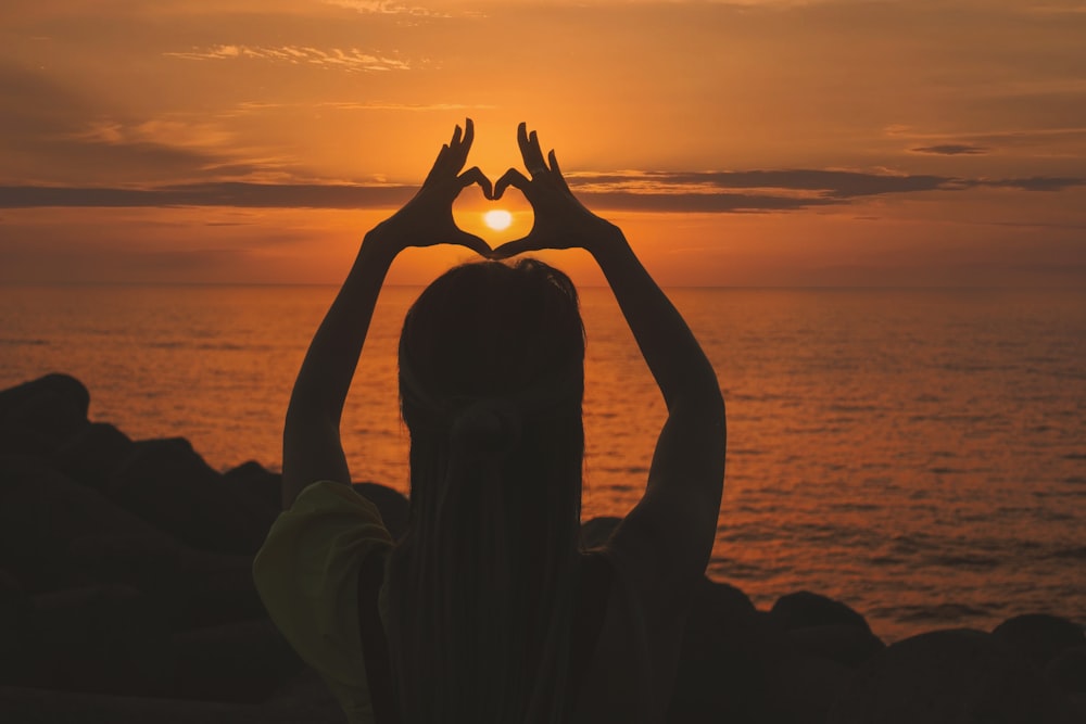 Silueta de mujer haciendo signo del corazón durante la puesta del sol