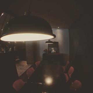 A warmly lit dining area with black chairs, white tables, and red pendant lights, creating an inviting atmosphere.