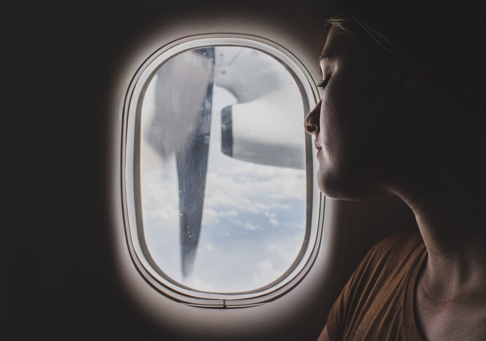 飛行中に就寝中に飛行機の窓の近くに座っている茶色のスクープネックを着た女性