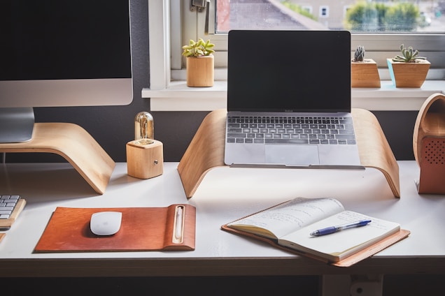 Modern office workspace with a laptop and notebook on a wooden desk.