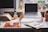 A modern office desk with a laptop and planner open, surrounded by plants and stationery.