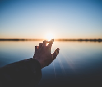 landscape photography of person's hand in front of sun