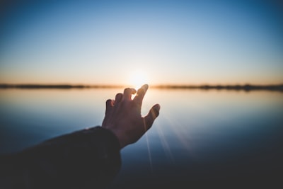 landscape photography of person's hand in front of sun hope teams background