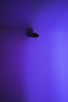 A grainy VHS-style image of a surveillance eye glowing turquoise against a stark black and gray background.