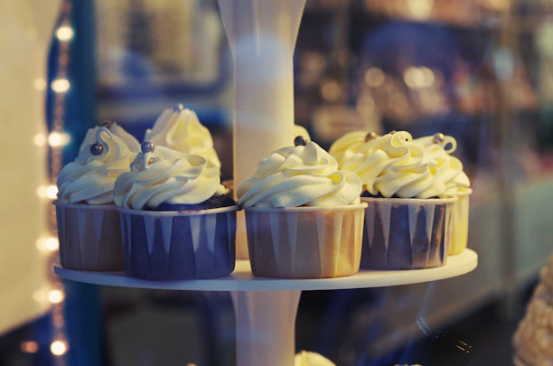 Elegant flat lay of luxury cupcakes with gold accents on a soft beige linen cloth, bathed in natural light.