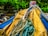 A close-up of a bundle of ropes intertwined and placed on a weathered yellow and blue fabric or tarp, set against a backdrop of green leaves and a wooden structure.