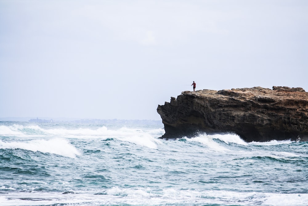 Mann steht auf einem Felsen und schaut auf das Meer