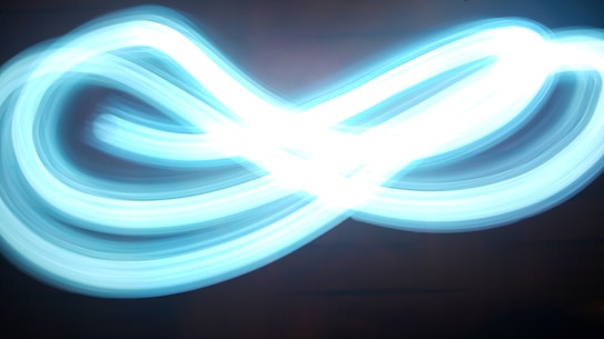 A bright, neon blue light creates an infinity loop pattern against a dark background, showcasing movement and energy.