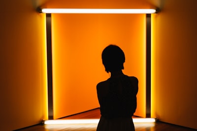 silhouette of woman standing in front of orange wall shape teams background