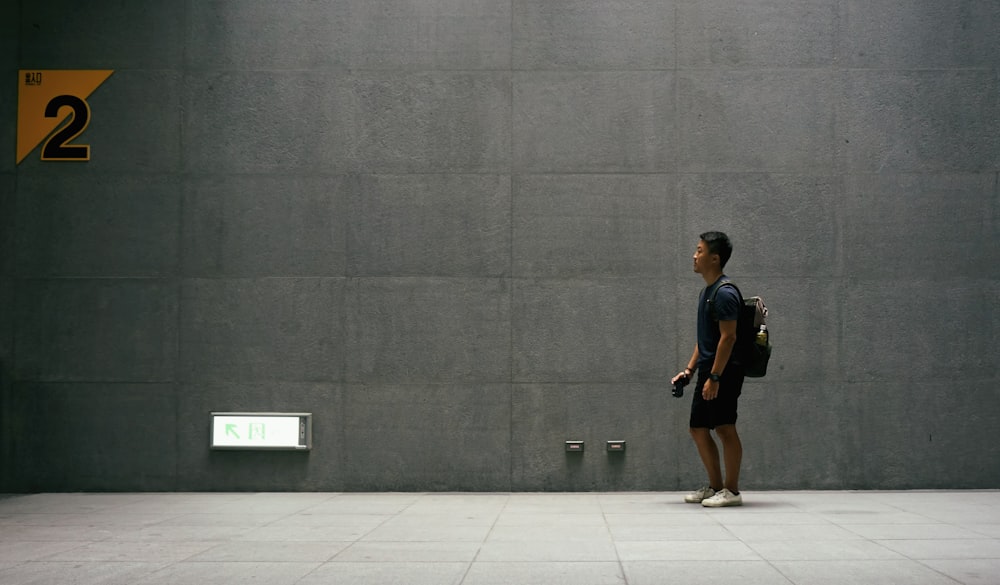 man in black top carrying backpack standing near wall