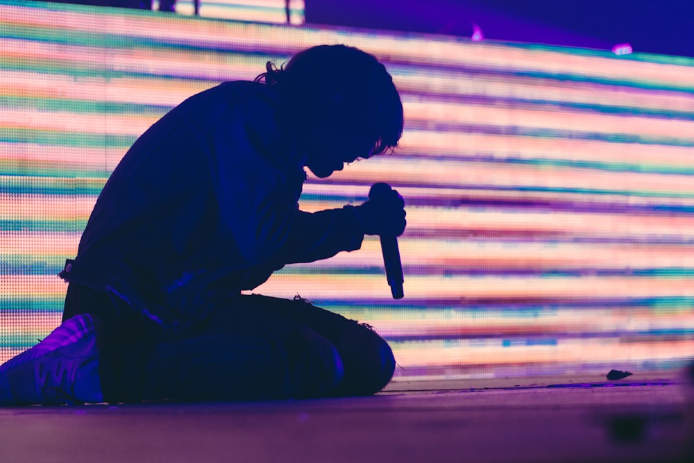 Silhouettenfoto eines Mannes, der auf der Bühne sitzt, während er ein dynamisches drahtloses Mikrofon in der Hand hält