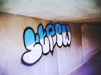 Graffiti art featuring stylized letters with a blue and white gradient outlined in black on a concrete wall.