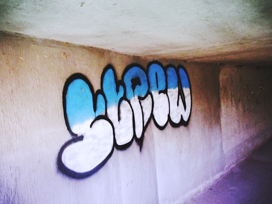 Graffiti art featuring stylized letters with a blue and white gradient outlined in black on a concrete wall.