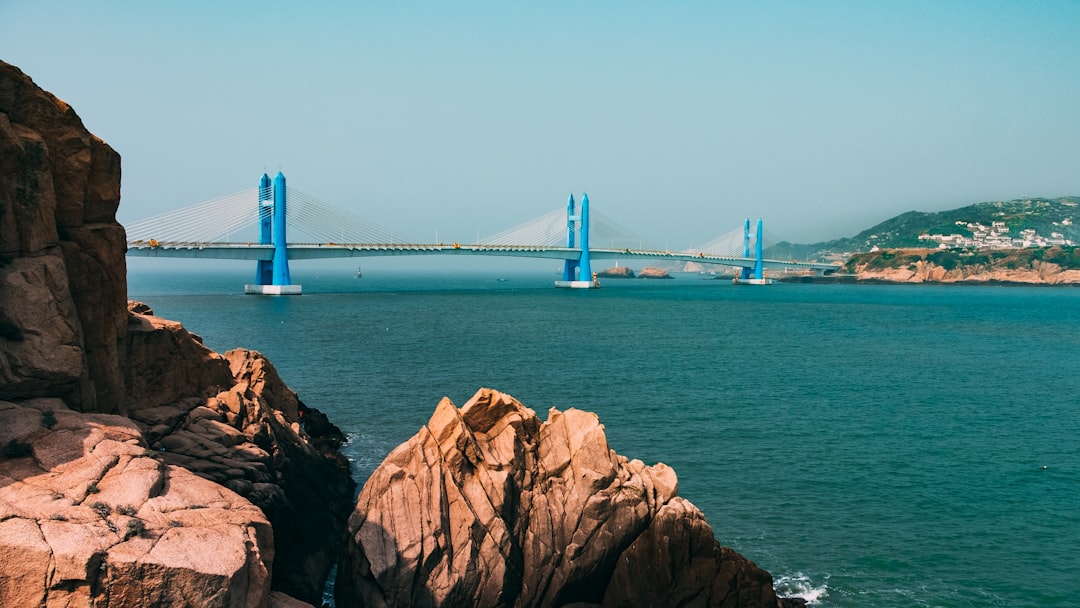 brown rock formation with blue and gray concrete bridge nearby above body of water