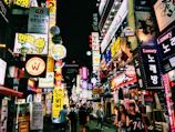 A bustling city street at night, glowing with neon signs and lively crowds.