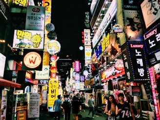 A bustling city street at night illuminated by colorful neon signs and lively crowds.